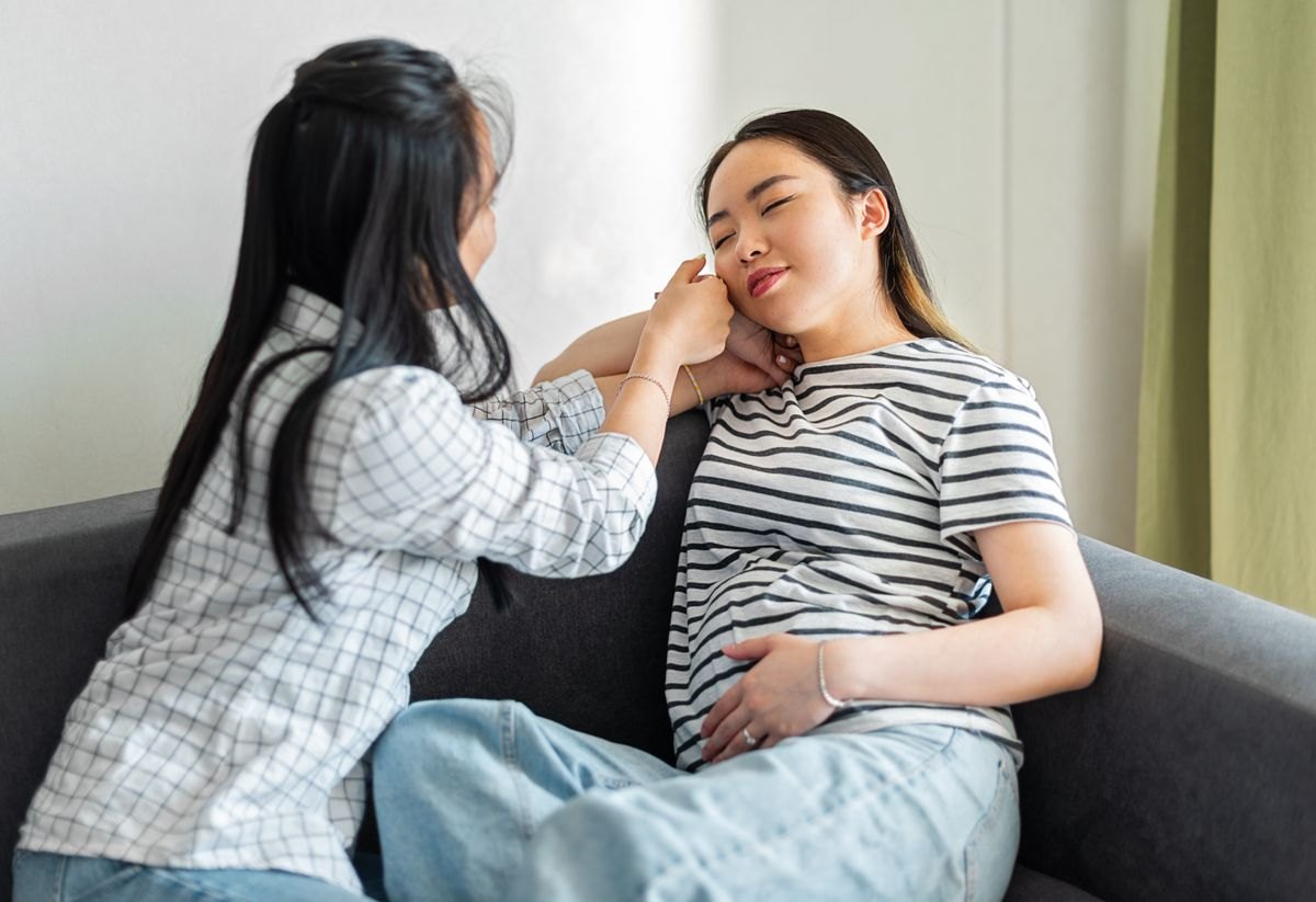 A companion offering comfort to a pregnant woman on a sofa