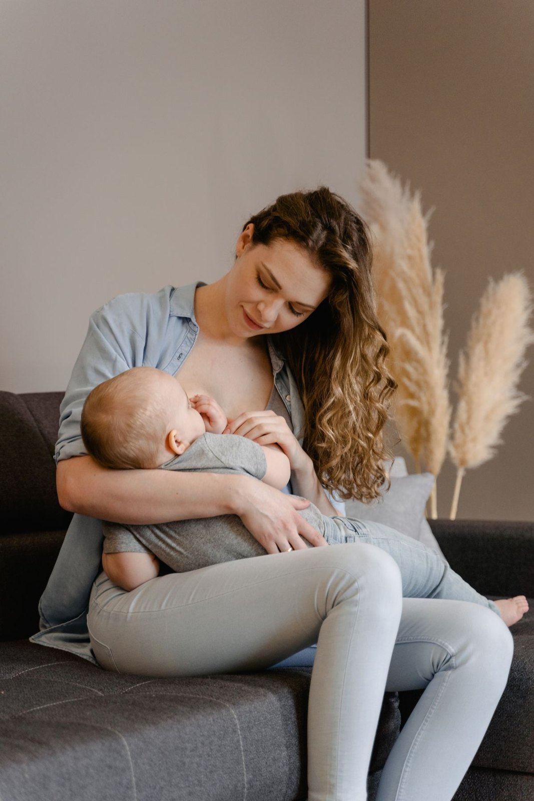 A parent feeding a baby while seated on a sofa at home